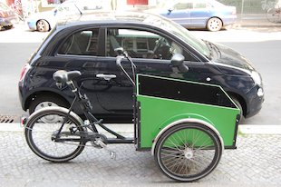 (das) Lieferfahrrad vor blauem Auto