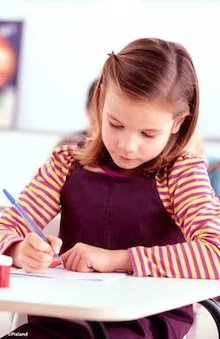 Primary aged girl sat at school desk writing