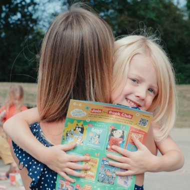Child hugging parent with Book Club leaflet