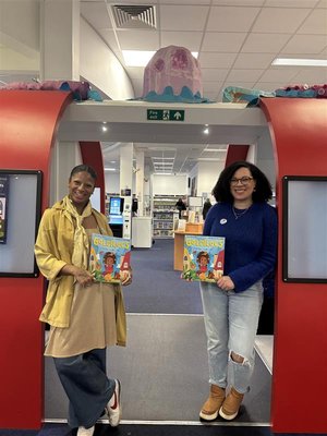 A photograph of Ella McLeod and Rochelle Falconer posing with their book, Goldilocs at a library in London.
